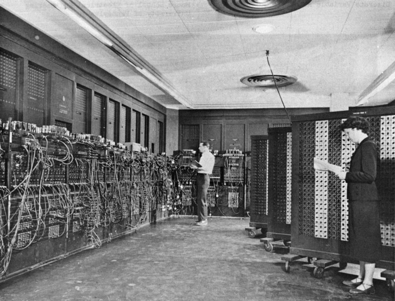 Two programmers setting switches on the ENIAC's long wall of panels